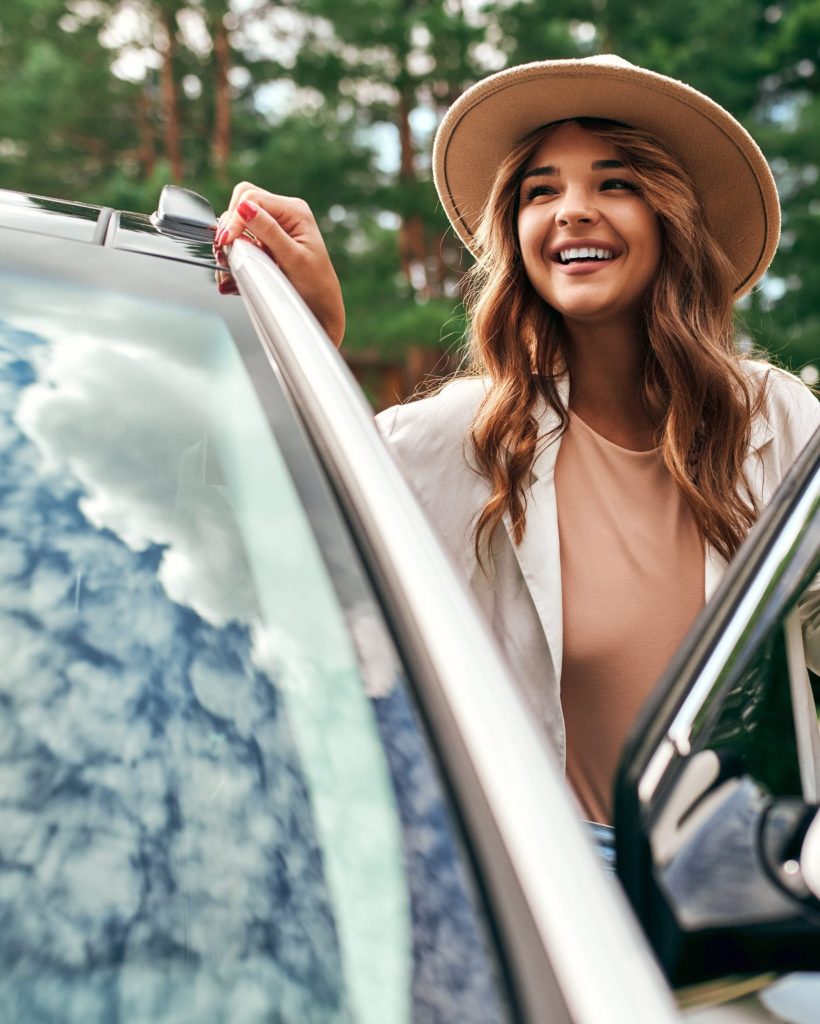 Jeune femme souriante sortant d'une voiture après une leçon de conduite réussie à l'auto-école de Genève, prête pour son permis de conduire suisse.